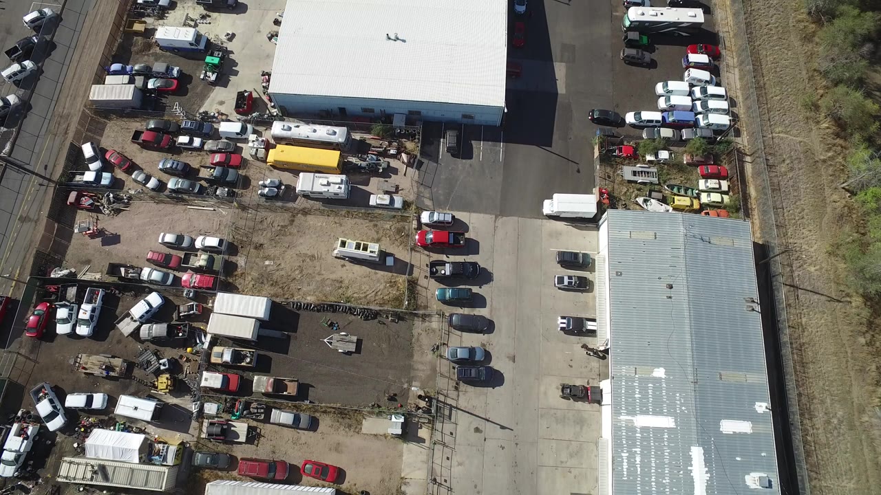 Overhead view of industrial buildings and parked vehicles beside dry grass.