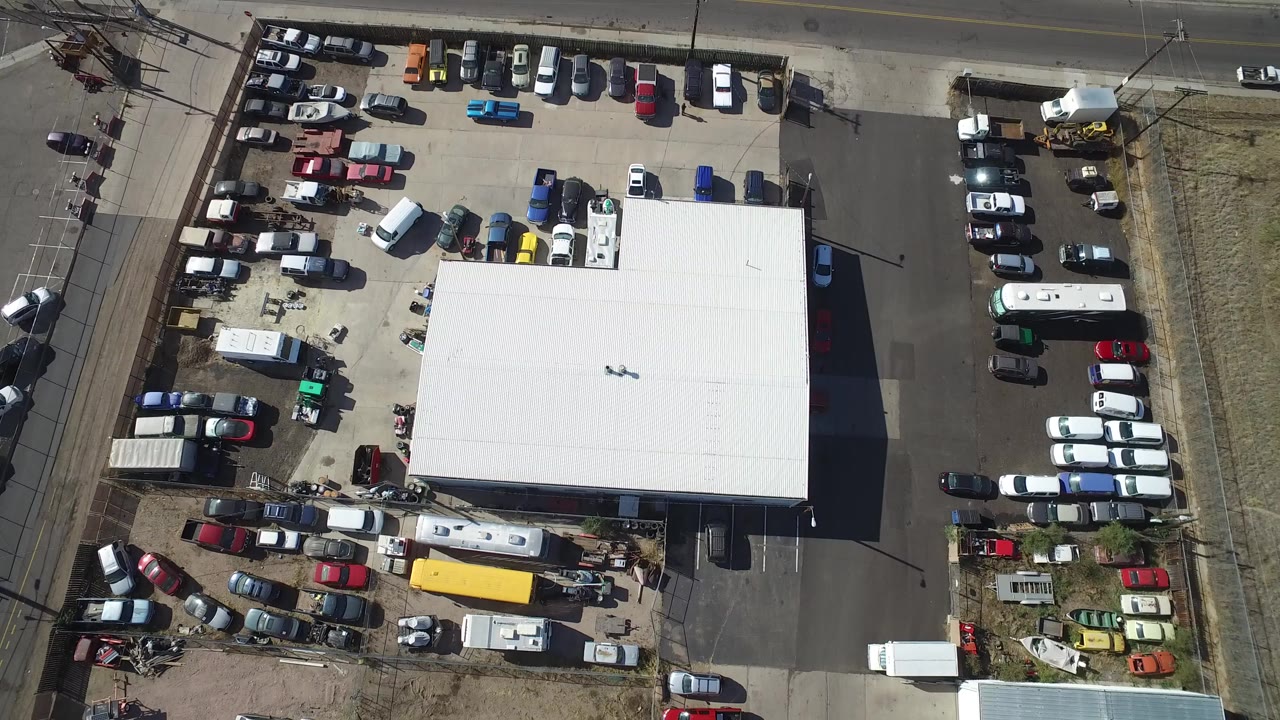 Overhead parking lot with a white-roofed building and rows of cars