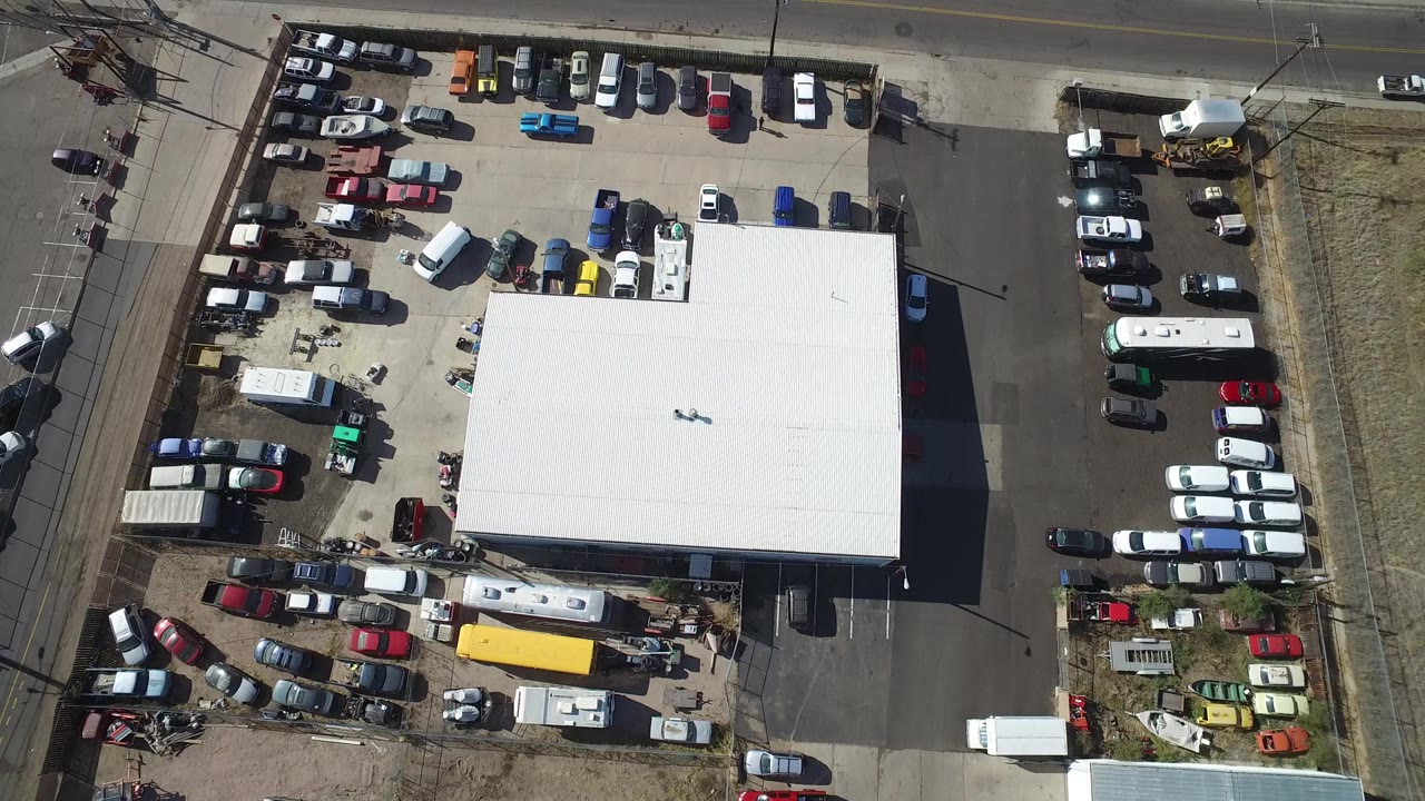 Aerial frame in Hidden Lake, Colorado with dense rows of parked cars around a white-roofed structure, a road along the top edge, and no visible people.