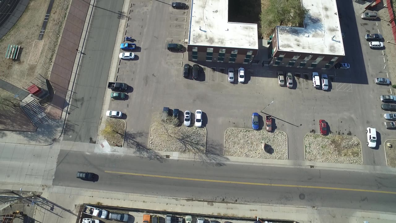 Second overhead frame in Hidden Lake, Colorado with the building shifted across the view, parking rows, a road at the bottom edge, and no visible people.