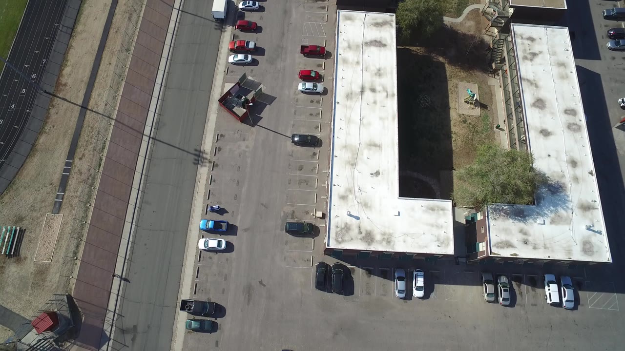 Overhead parking lot beside flat-roof buildings and a broad road.