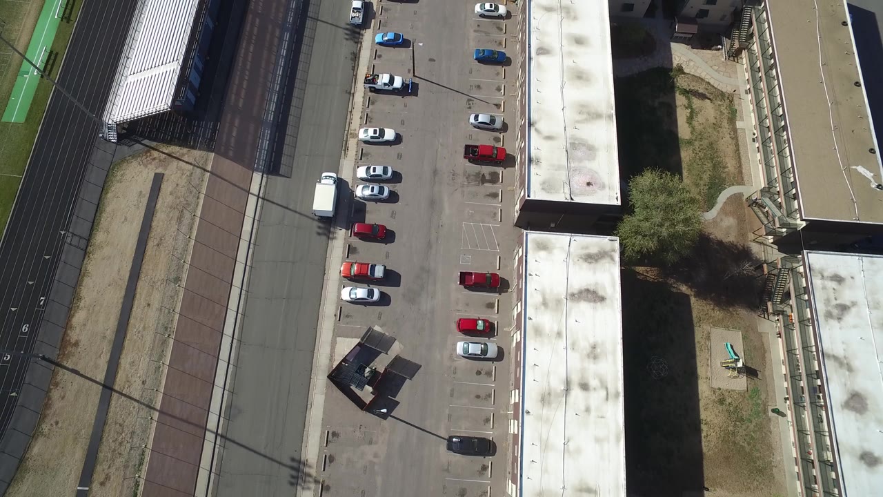 Top-down aerial view of a parking lot beside buildings and track lanes.