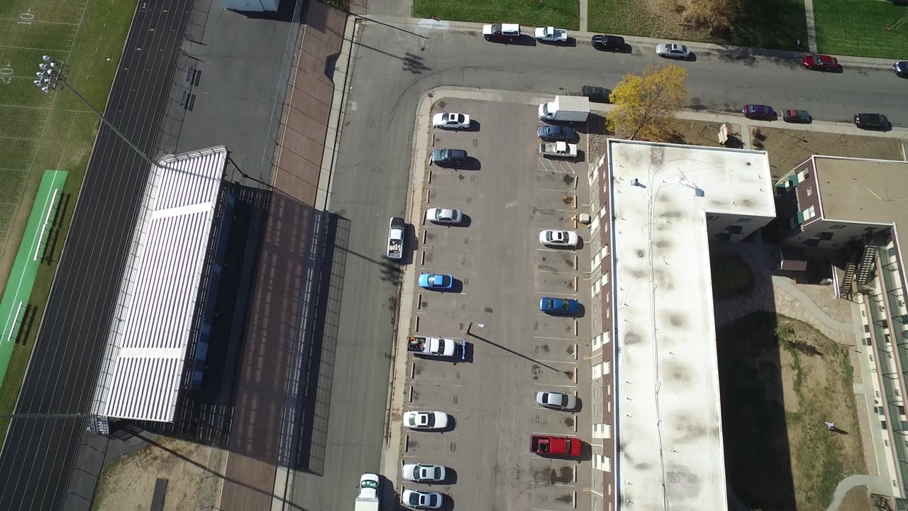 Drone view over parked cars, a road, and a field edge.