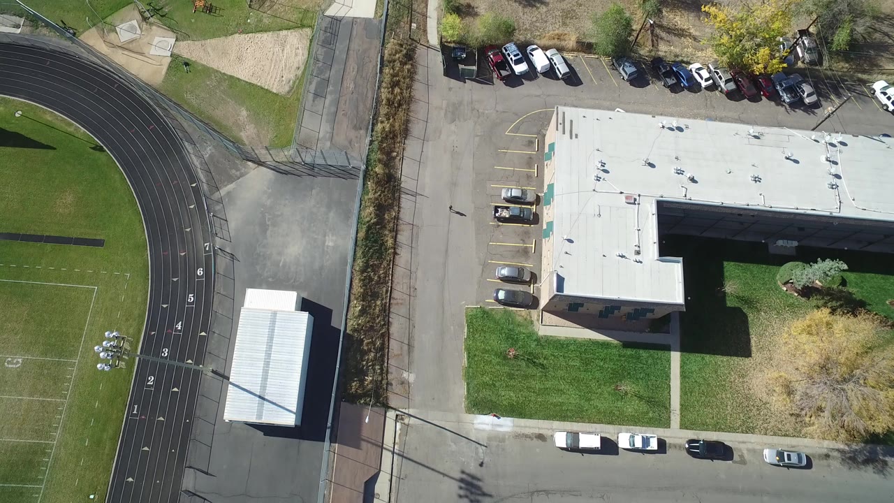 Overhead view of a white-roofed building beside a track and roadway.