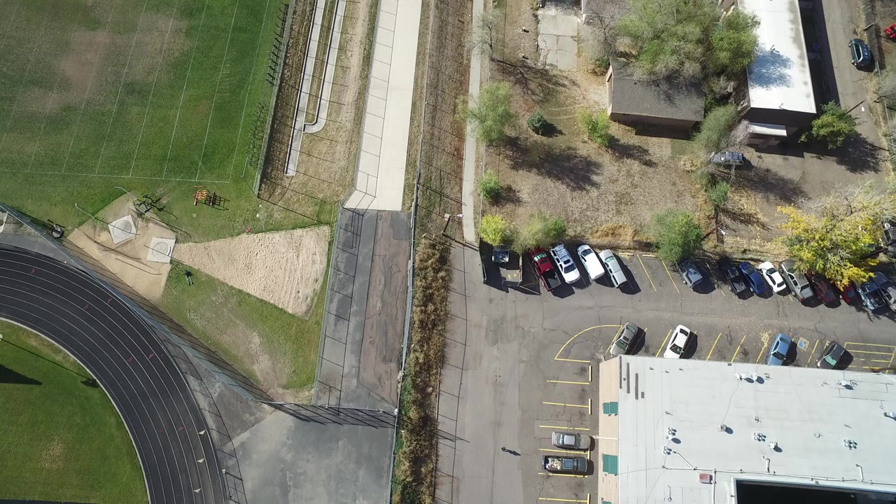 Top-down aerial view of a football field beside a running track, road, parking lot, and buildings.