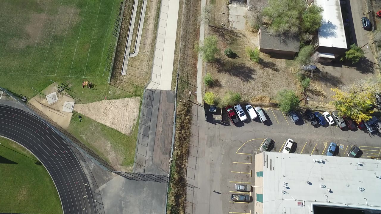 Aerial view in Hidden Lake, Colorado, with more of the parking area and rooflines centered beside the marked green football field and black running track, with no visible people.
