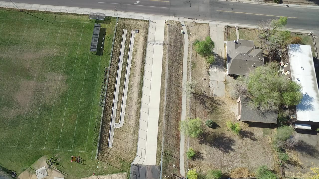 Second overhead frame in Hidden Lake, Colorado with the road across the top, a marked green field, metal bleachers, sidewalks, trees, and homes with no visible people.