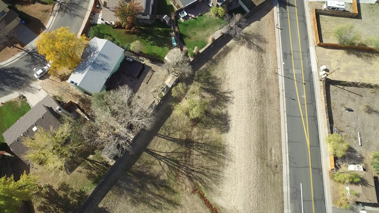 High overhead view in Hidden Lake, Colorado showing rooftops, fenced yards, trees, a two-lane road, and dry ground, with no clearly identifiable people visible.