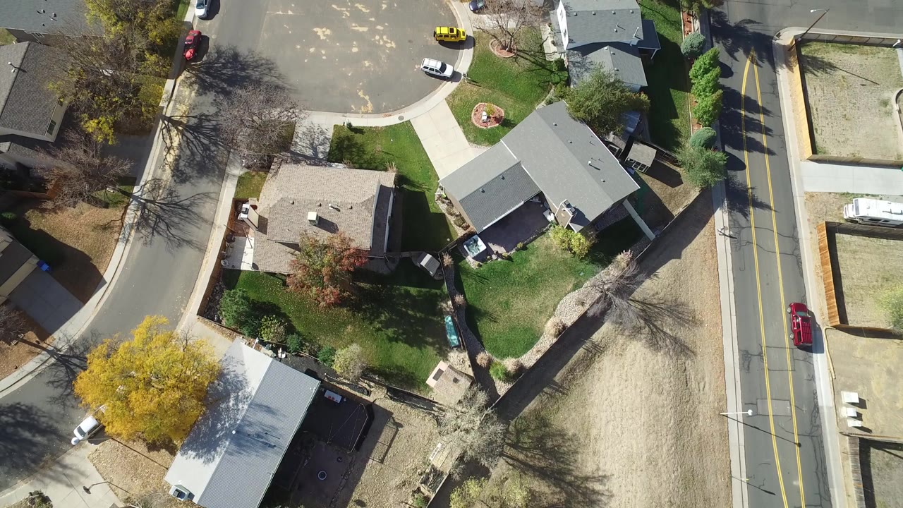 Overhead view of suburban homes, lawns, streets, and parked cars.