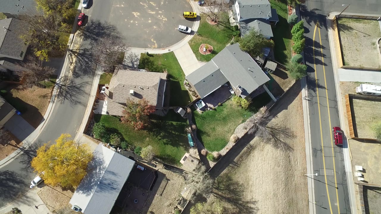 Hidden Lake, Colorado aerial frame with gray rooftops, fenced yards, parked vehicles, a curved street corner, a yellow car near the upper road, and no visible people.