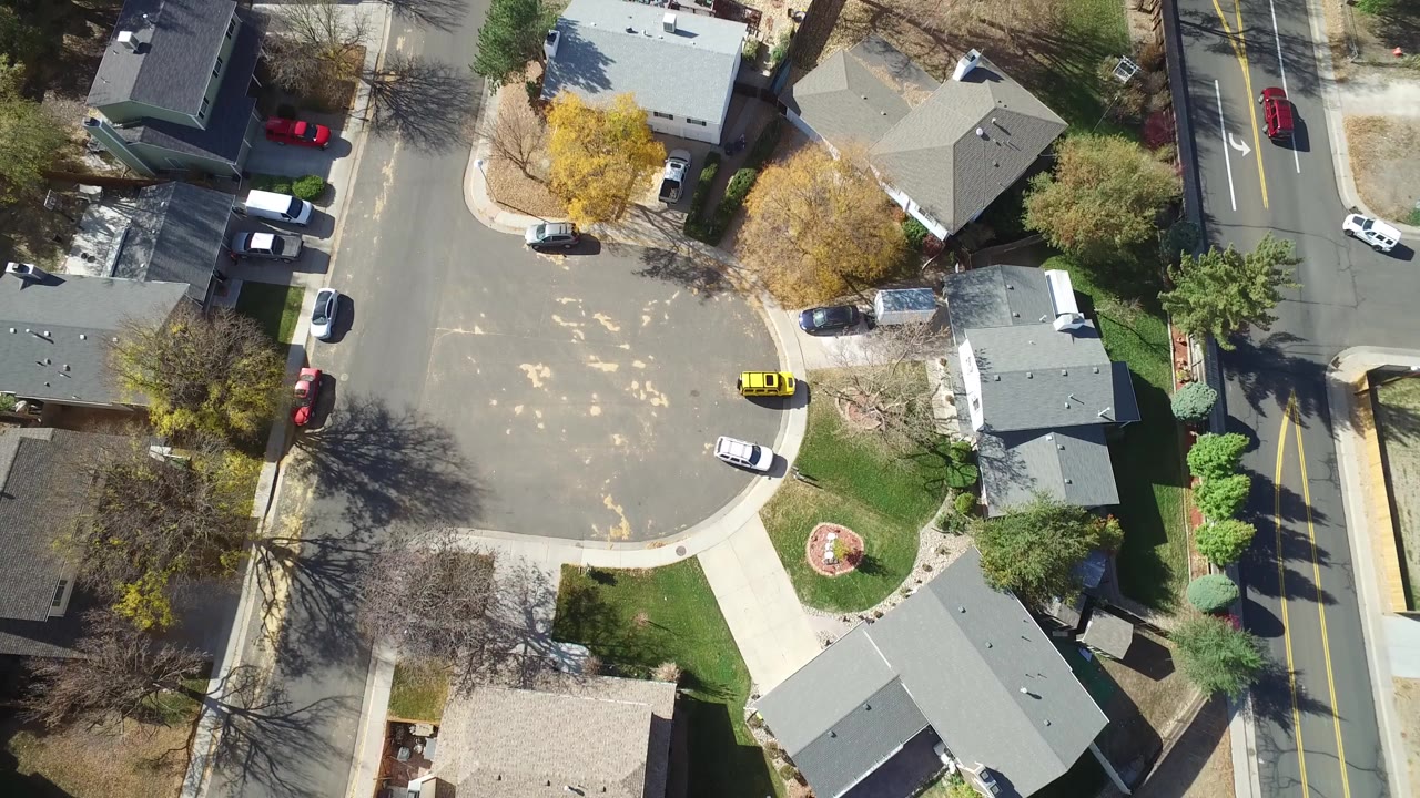 Overhead view of a residential cul-de-sac with homes, parked cars, trees, and a road.