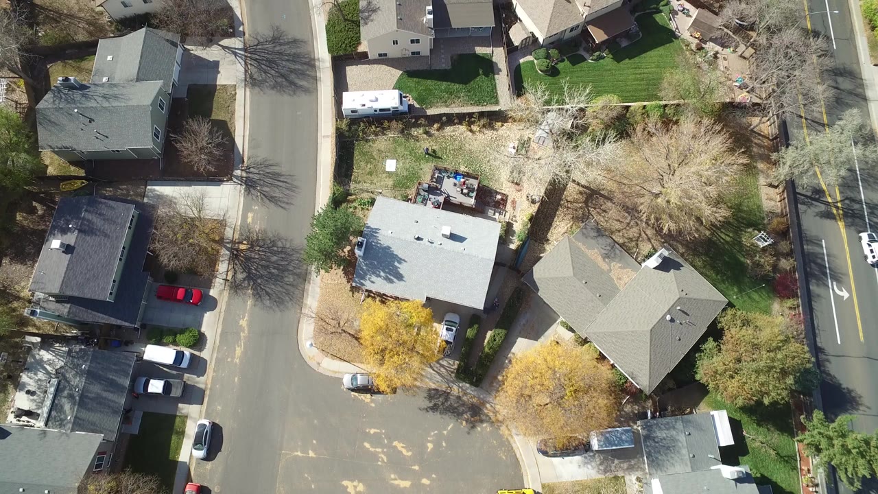 Overhead view of suburban houses, lawns, streets, and parked cars.