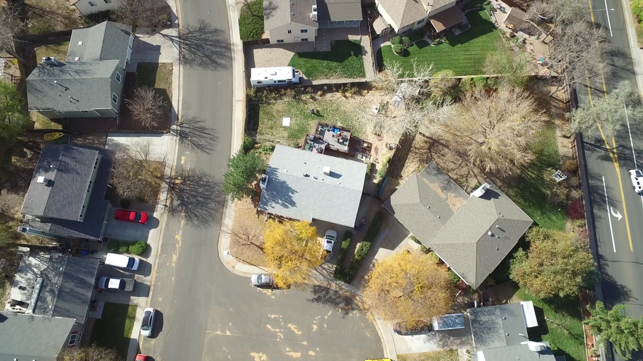 Aerial view over Hidden Lake, Colorado rooftops and yards, with a white vehicle in a driveway, a red car near the lower left, roadside lanes at the right edge, and no visible people.