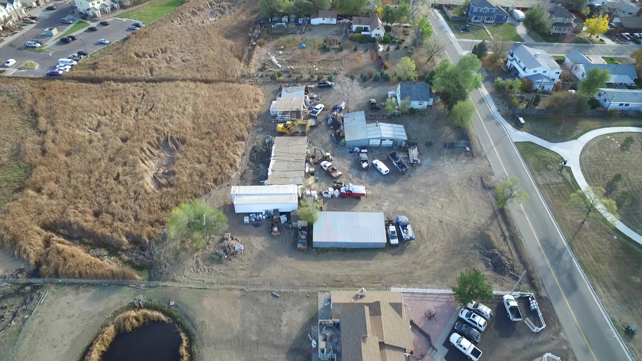 High angle view of field, storage yard, warehouses, vehicles, and neighborhood homes.