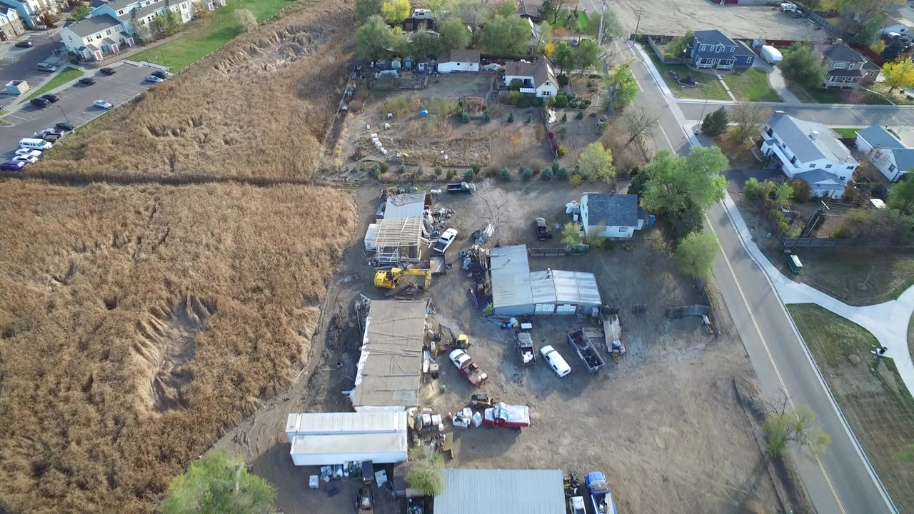 Aerial view of dry field, rough yard, sheds, vehicles, and nearby road.
