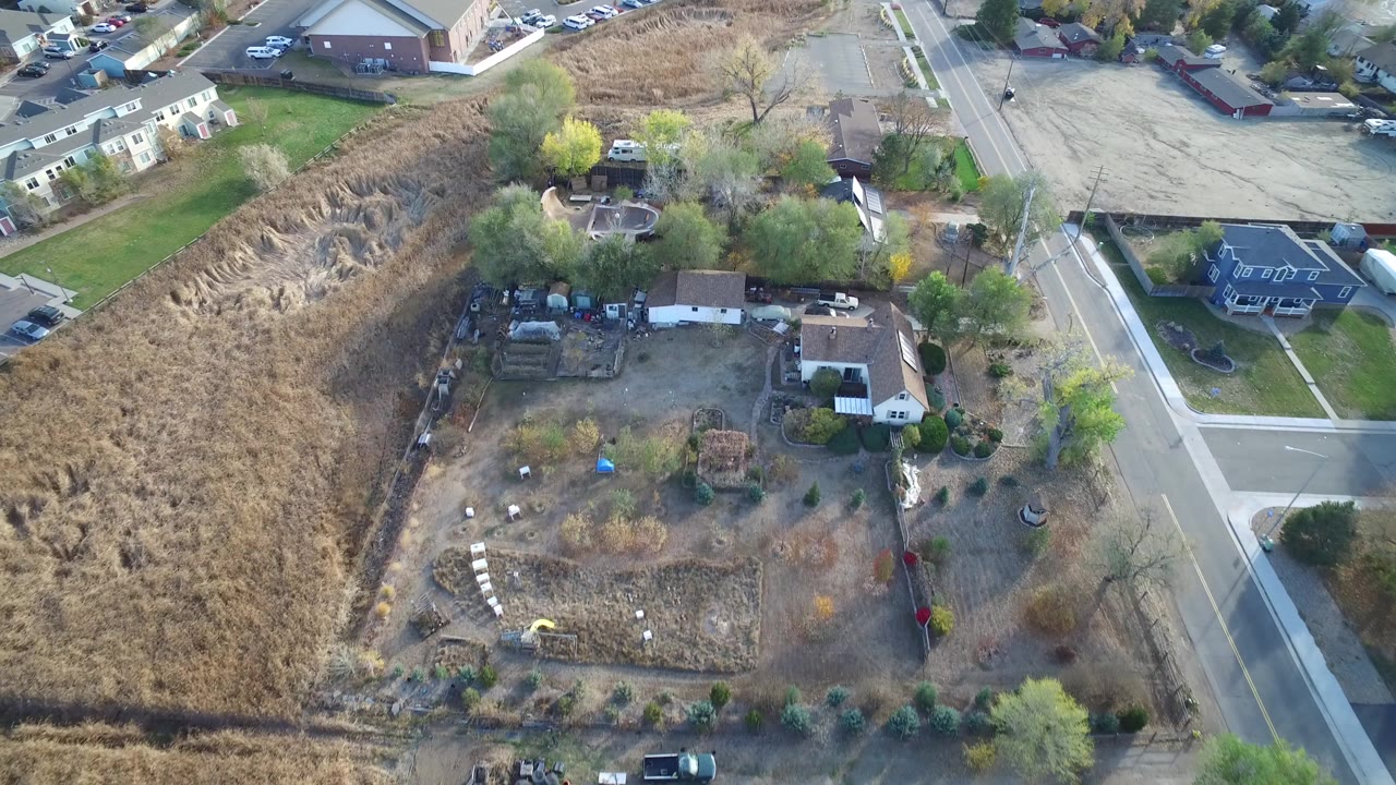 Aerial frame over Hidden Lake, Colorado showing a house with a large backyard beside a brown open field, nearby streets, parked cars, and no visible people.