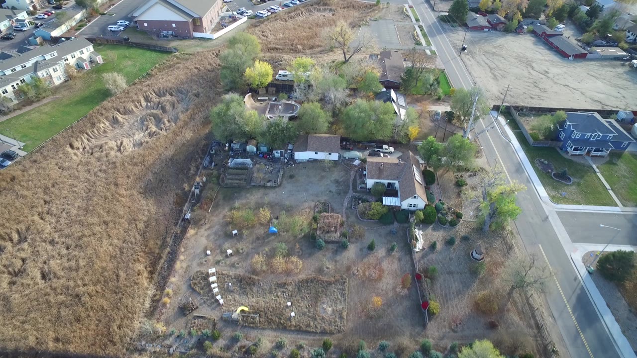Drone-style view of a house lot, brown field, and suburban intersection.
