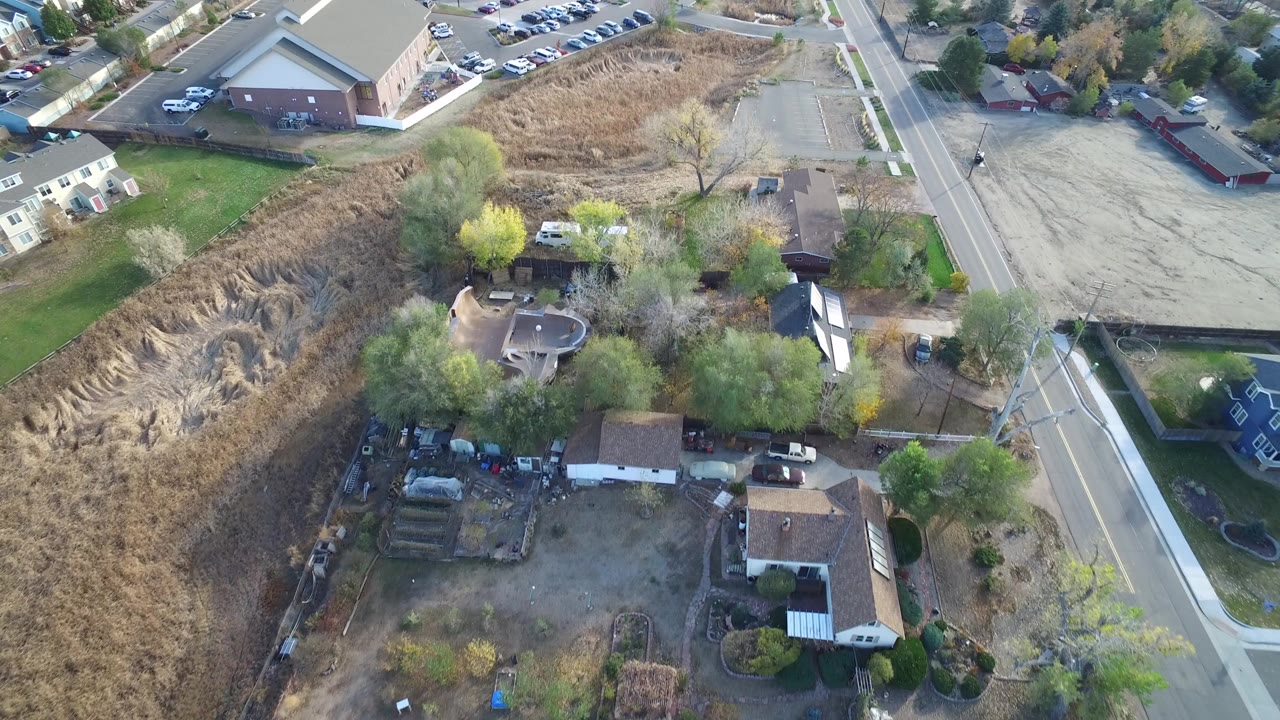 Overhead view of homes, open grass, roads, and a parking lot.
