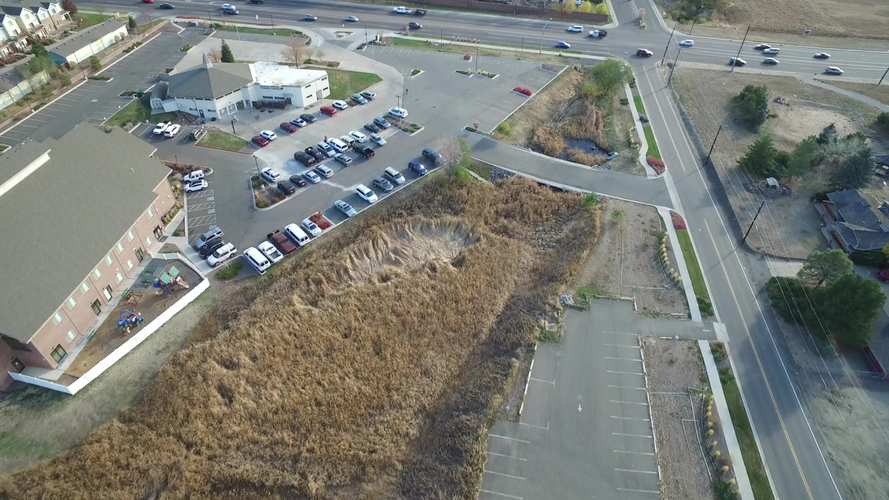 Aerial frame of dry grass, a parking lot, and nearby road traffic.