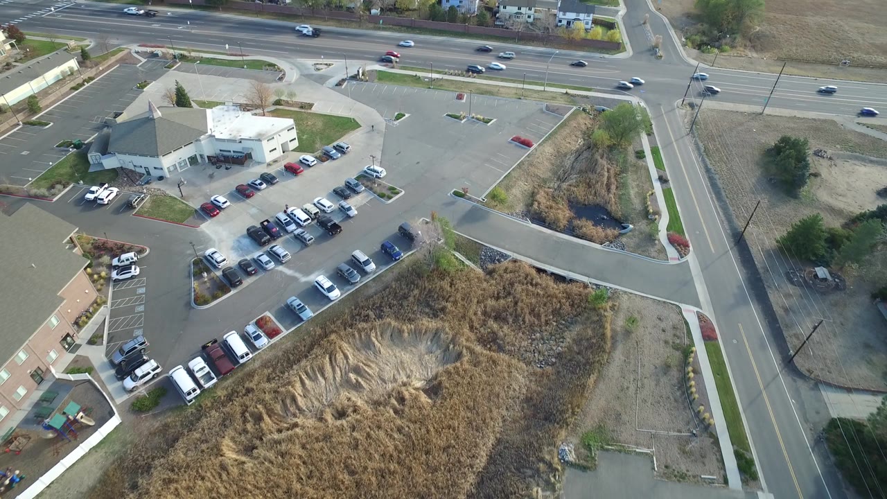 Aerial view in Hidden Lake, Colorado, with the building and parked cars centered left, a broad road crossing the top, a side street at right, and no visible people.