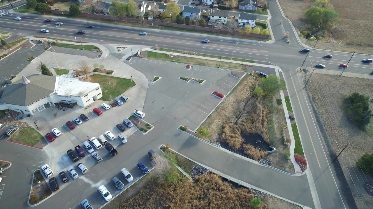 Overhead view of a commercial building, parking lot, road traffic, and nearby homes.