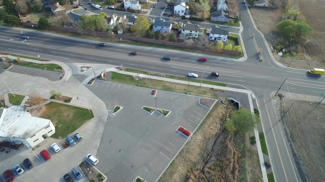 Aerial frame over Hidden Lake, Colorado showing a multi-lane road, a side street, a mostly empty parking lot, houses, trees, and no visible people at the start of the clip.