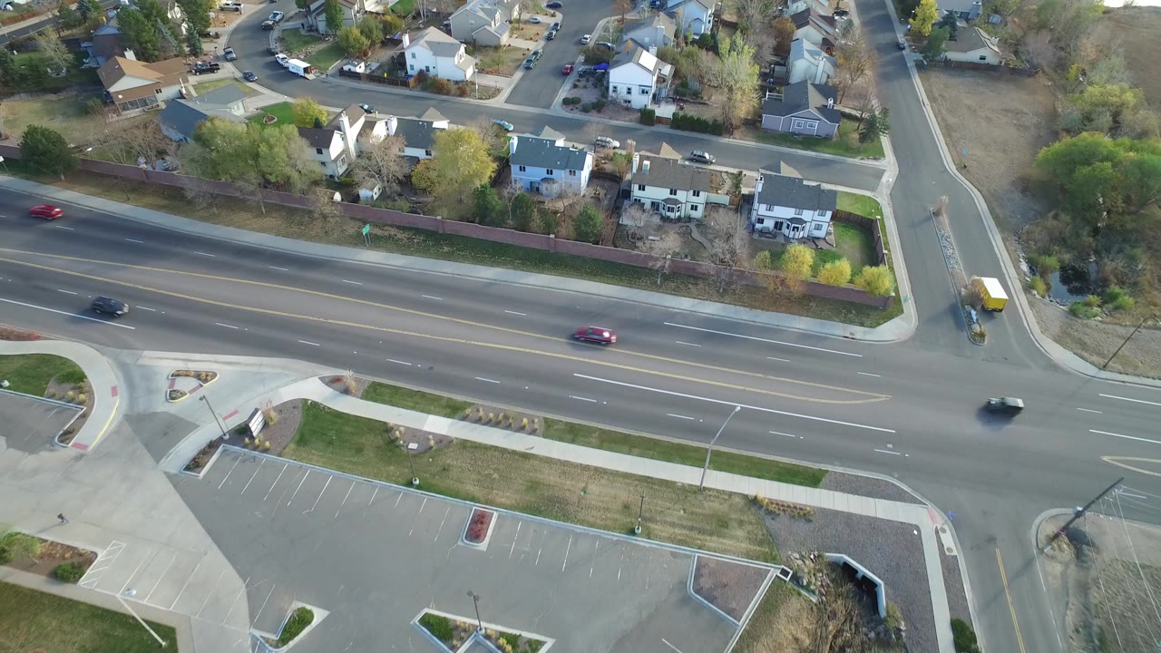 Aerial view of cars on a multi-lane road beside houses and a parking lot.