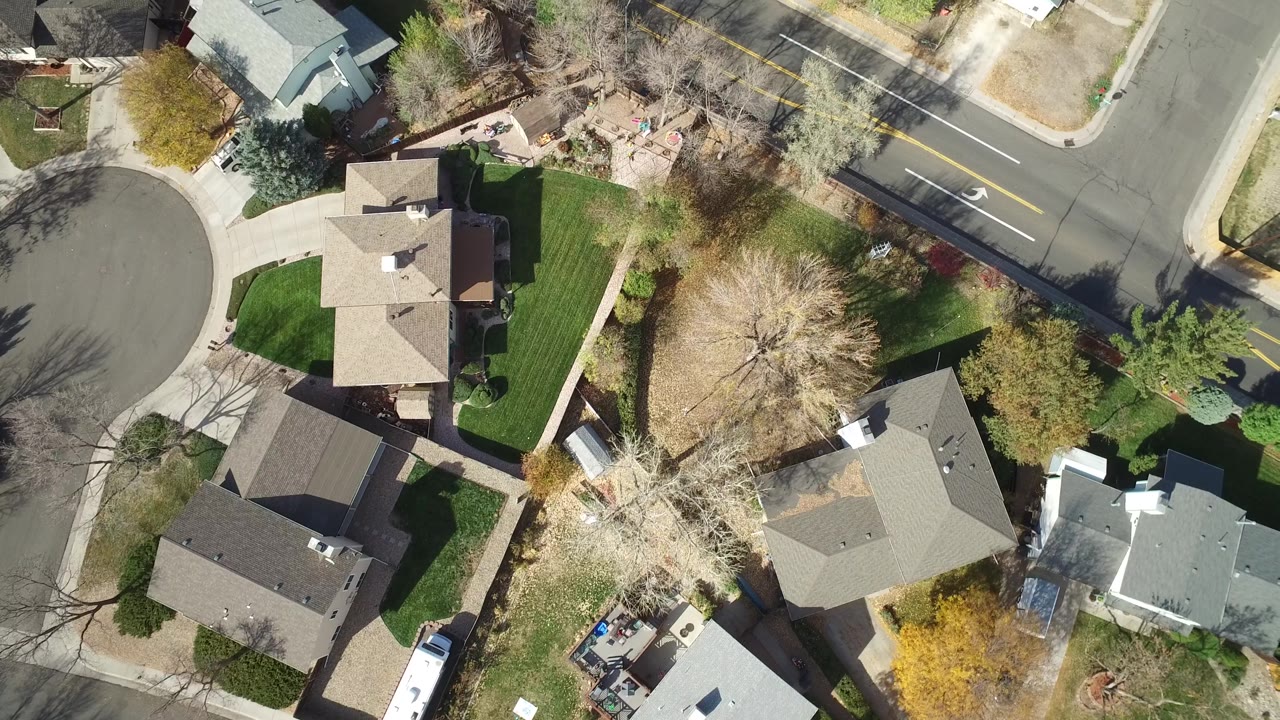 Aerial view in Hidden Lake, Colorado with a cul-de-sac on the left, rooftops in the center, a larger road at the top, yards, sidewalks, and no visible people.
