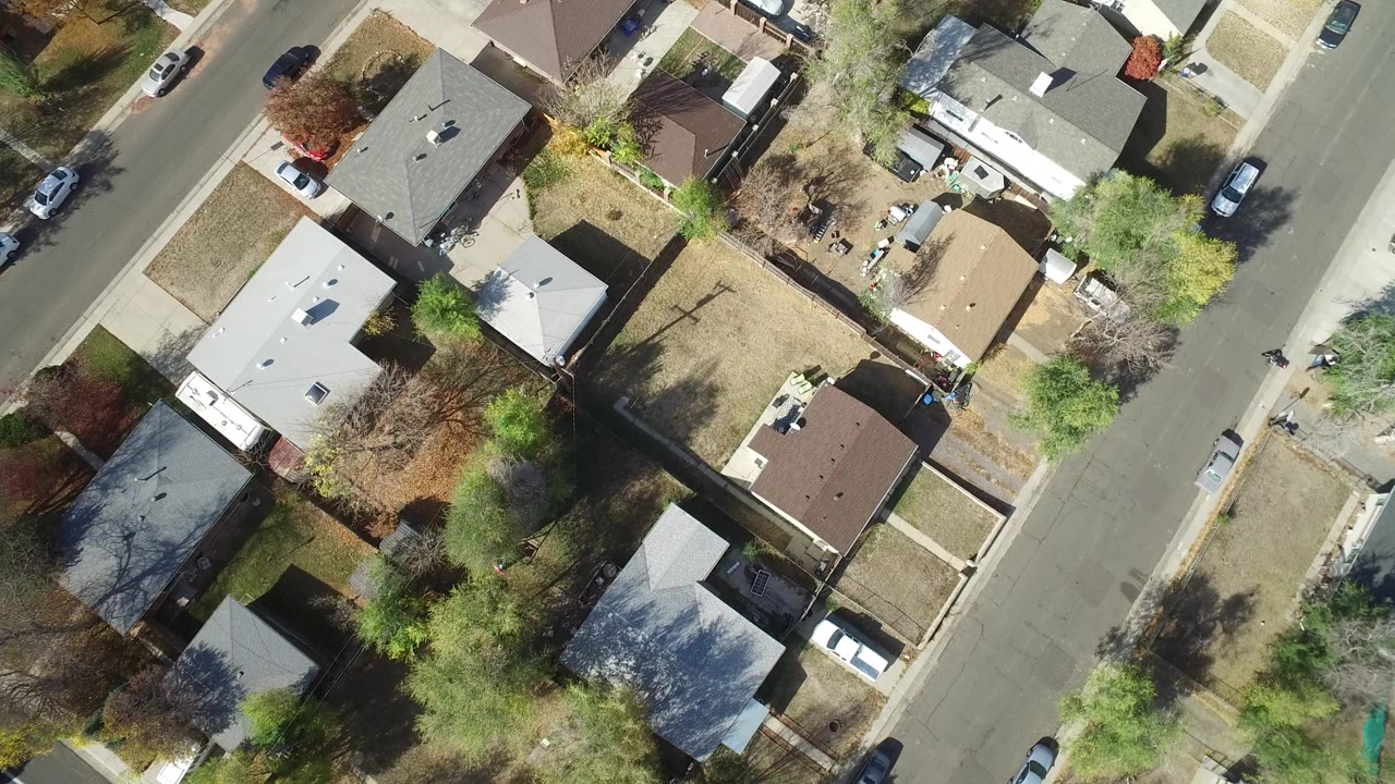 Top-down aerial view of homes, yards, a residential road, trees, and cars.