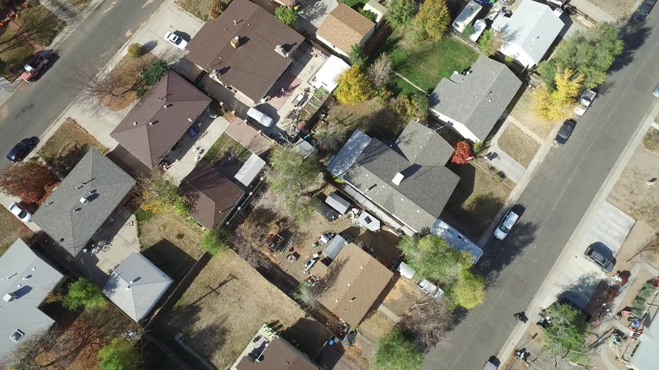 Aerial frame over Hidden Lake, Colorado with rooftops across the center, a straight residential road along the right side, small yards, trees, driveways, and no visible people.