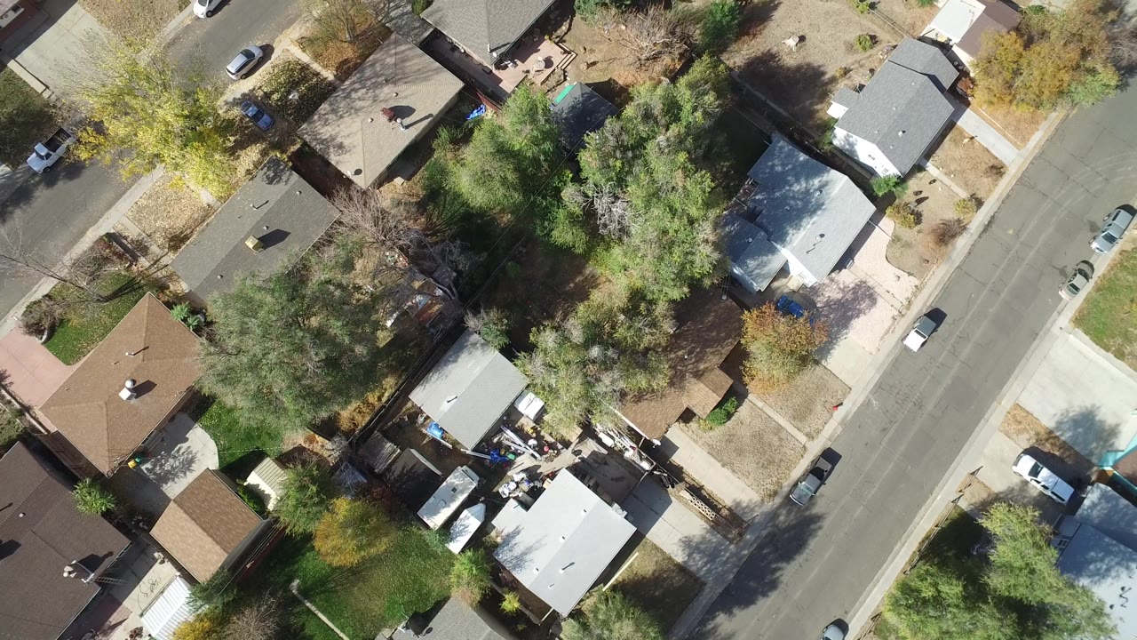 Second overhead frame in Hidden Lake, Colorado with gray and brown rooftops, mature trees casting shadows, dry yards, parked cars, and no visible people.