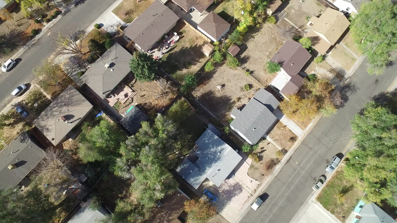 Top-down aerial frame over Hidden Lake, Colorado homes, fenced yards, parked cars, and tree shadows, with no visible people.