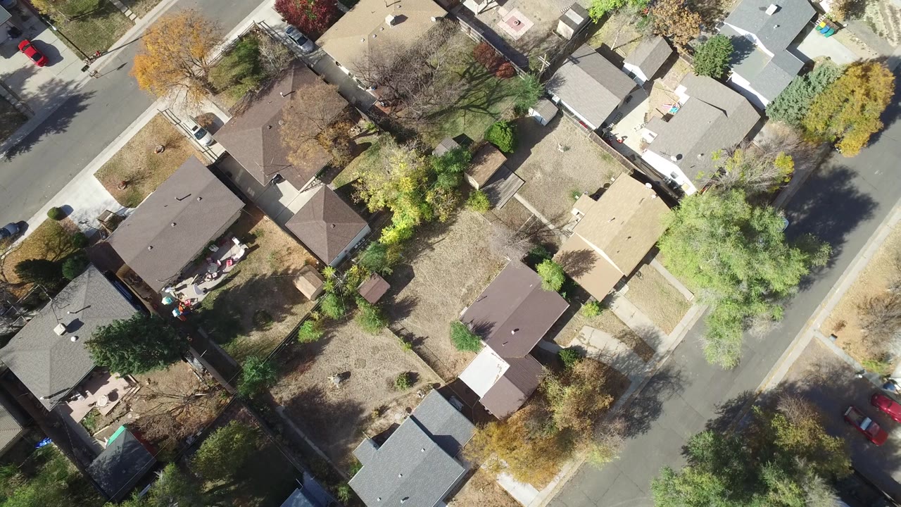 Second overhead frame in Hidden Lake, Colorado showing brown and gray rooftops, dry lawns, leafy trees, paved streets, parked vehicles, and no visible people.