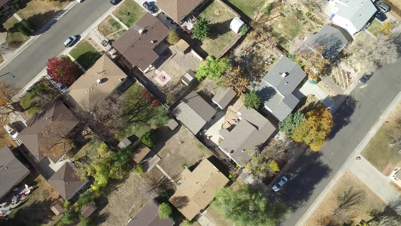 Overhead aerial frame of Hidden Lake, Colorado homes with diagonal streets, fenced yards, trees in mixed green and autumn colors, parked cars, and no visible people.