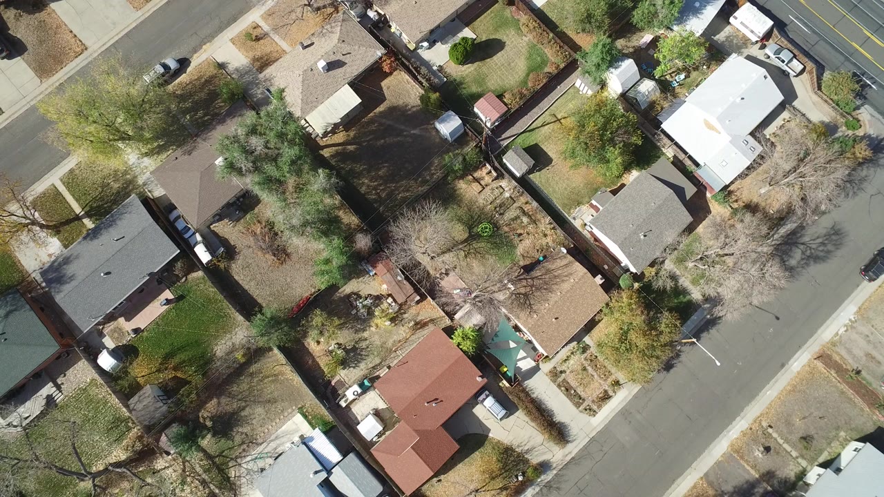 Top-down aerial view of small homes, yards, trees, and a residential street.
