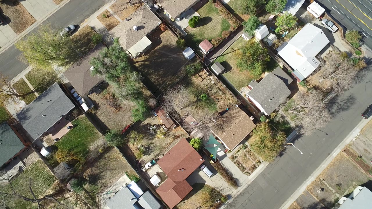 Overhead frame in Hidden Lake, Colorado, with tan and red-roofed one-story houses, fenced backyards, dry grass, trees, and cars along the curb.