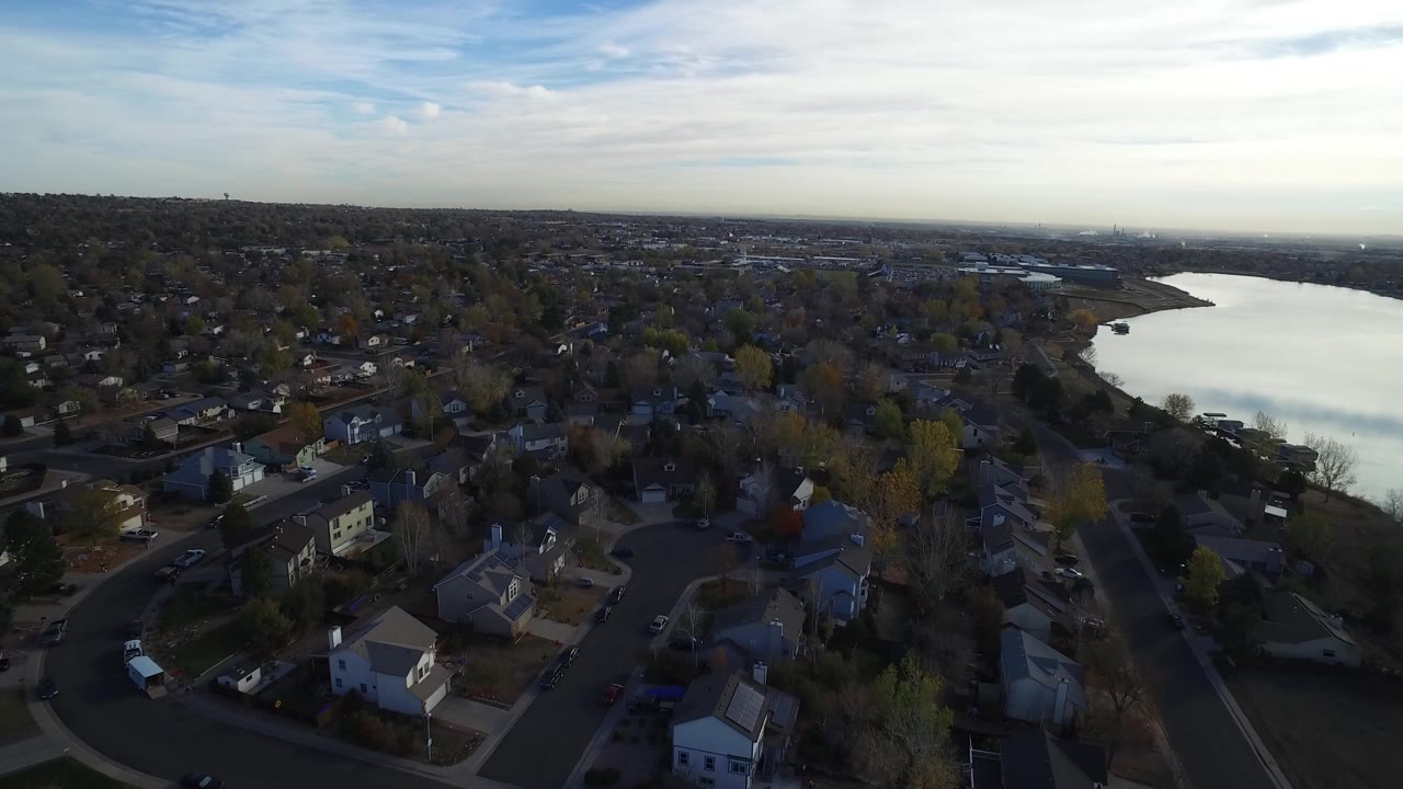 High aerial view over Hidden Lake, Colorado with residential rooftops in the foreground, a bright lake on the right, distant development on the horizon, and no visible people.