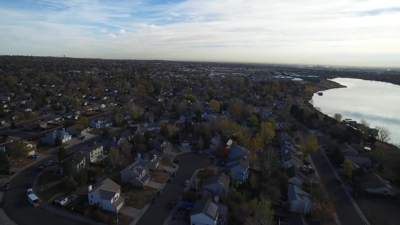 Drone-height view of rooftops, streets, trees, and a reflective lake.