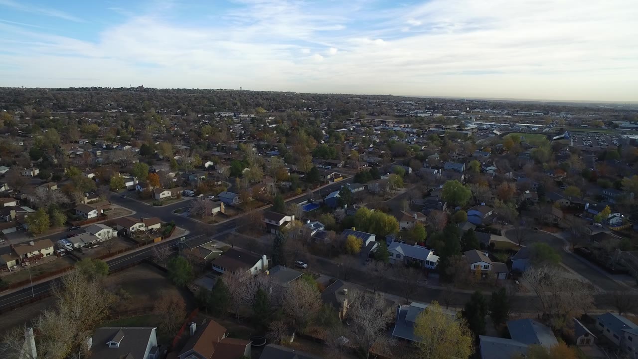 Aerial frame over Hidden Lake, Colorado showing rooftops, intersecting residential streets, mixed bare and green trees, broad sky, and no visible people.