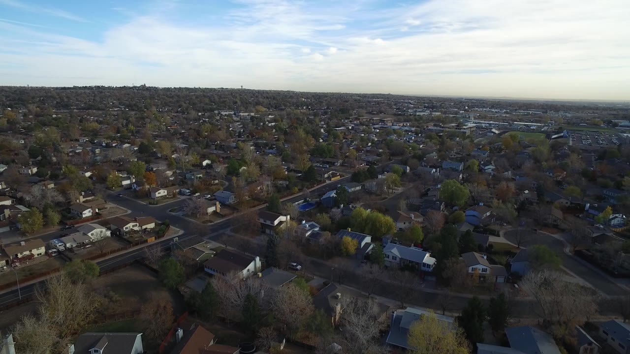 Drone-height view across houses, trees, roads, and distant suburban blocks.