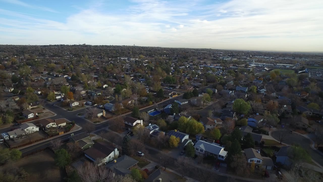 Aerial view over a residential neighborhood with streets, houses, trees, and a wide sky.