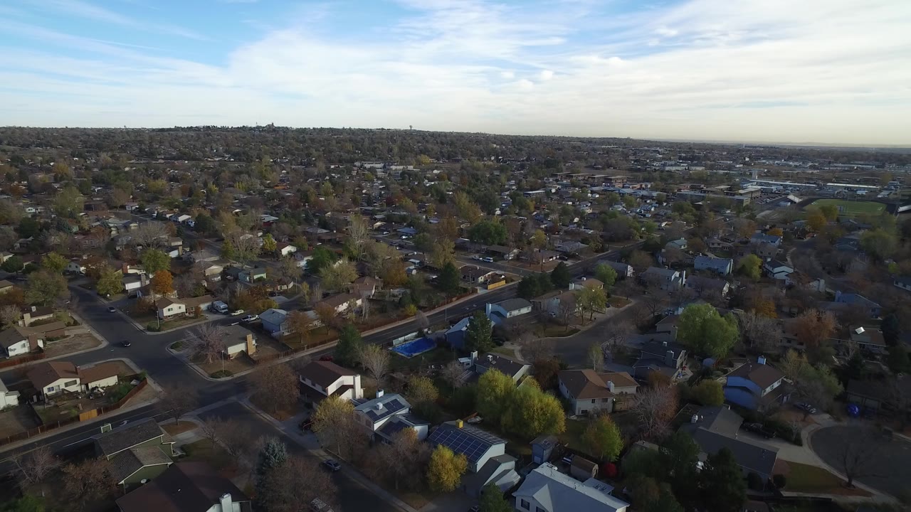 Aerial view over suburban homes and tree-lined streets under a blue sky.