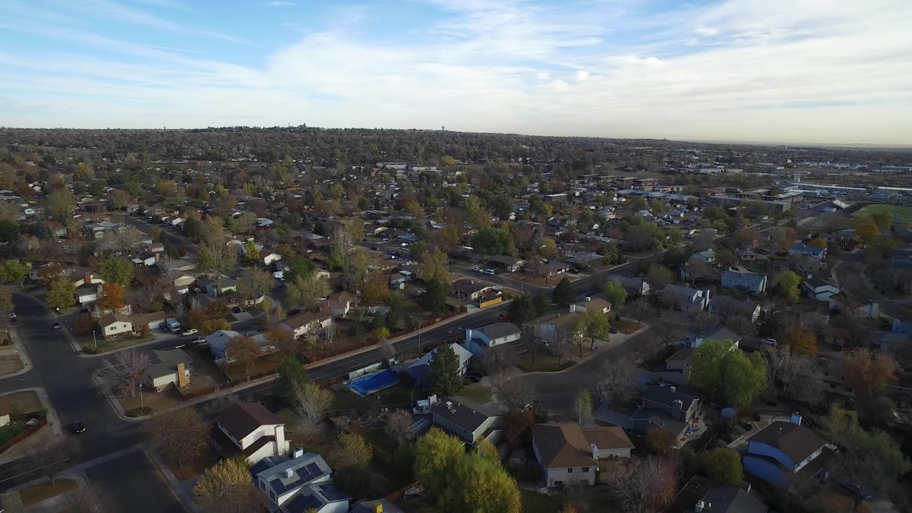 Aerial view over suburban houses, roads, trees, and a wide sky.