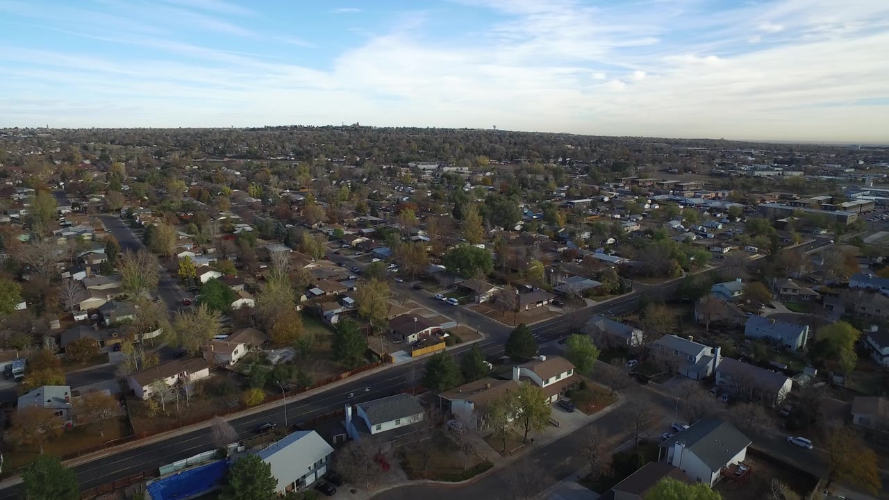 Aerial view of suburban houses, streets, trees, and blue sky.