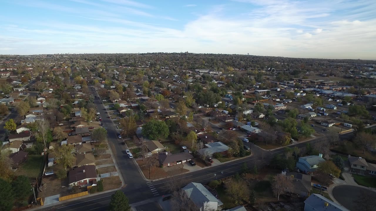 High aerial view of Hidden Lake, Colorado showing rows of houses, tree-lined streets, a foreground intersection, distant neighborhoods, and no visible people.