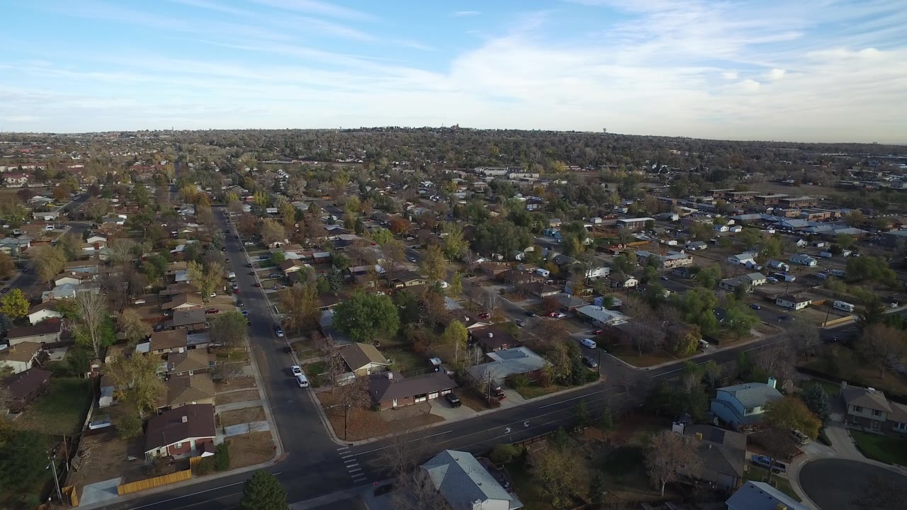Drone view across suburban rooftops, streets, trees, and distant horizon.