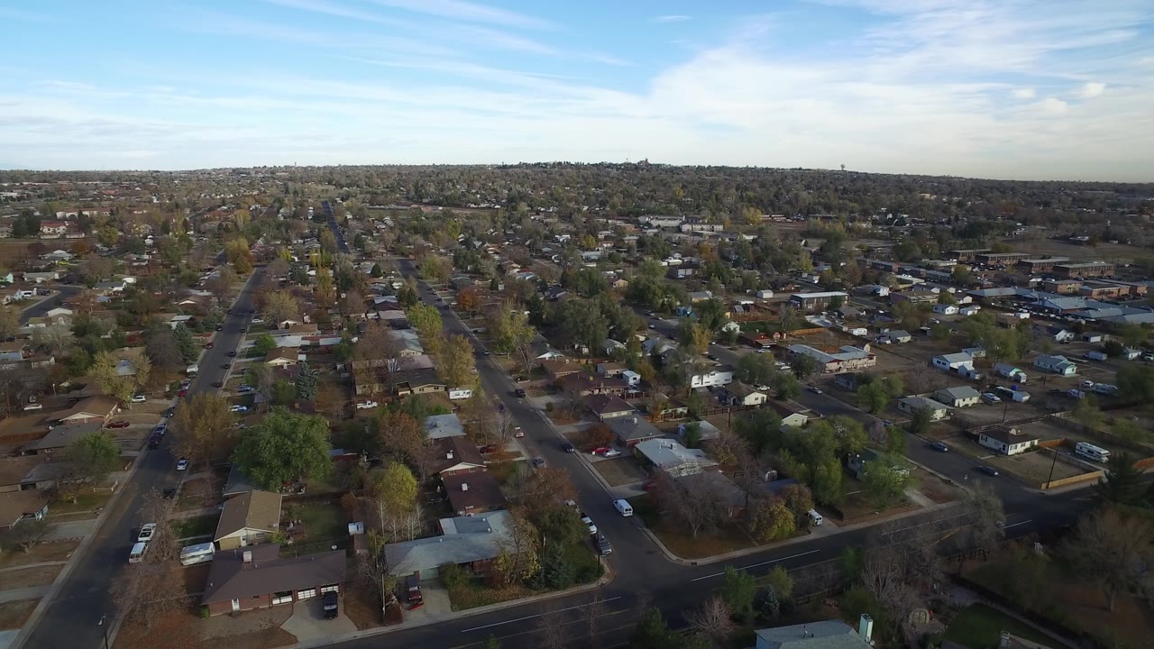 Aerial view in Hidden Lake, Colorado, centered on a long straight residential road, with rooftops, yards, trees, and no visible people.