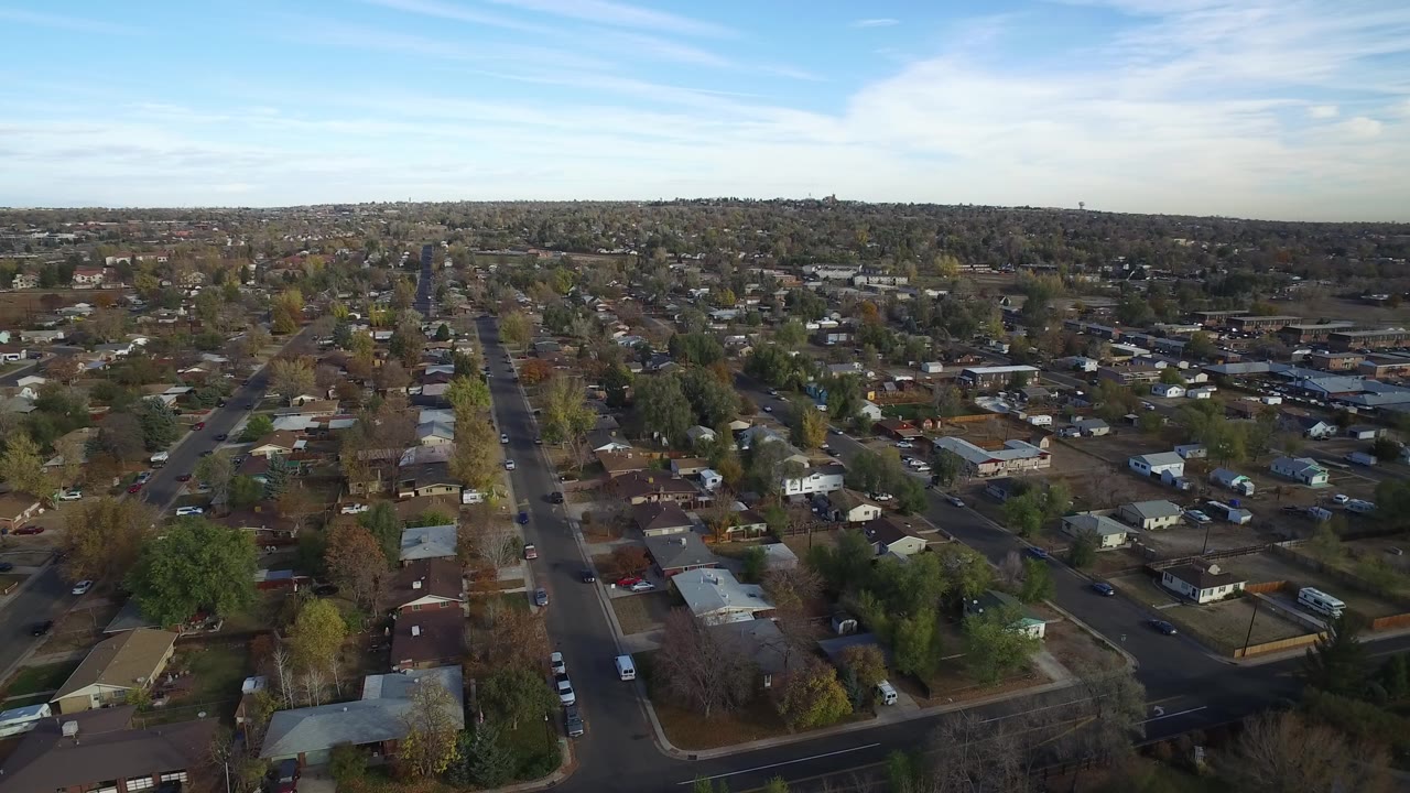 Aerial view over straight suburban streets and homes under a blue sky.