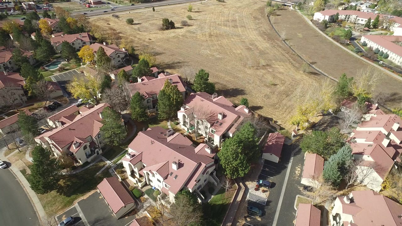 Opening aerial frame over Hidden Lake, Colorado showing red-roofed residential buildings, curved streets, trees, and a dry field beyond, with no visible people.