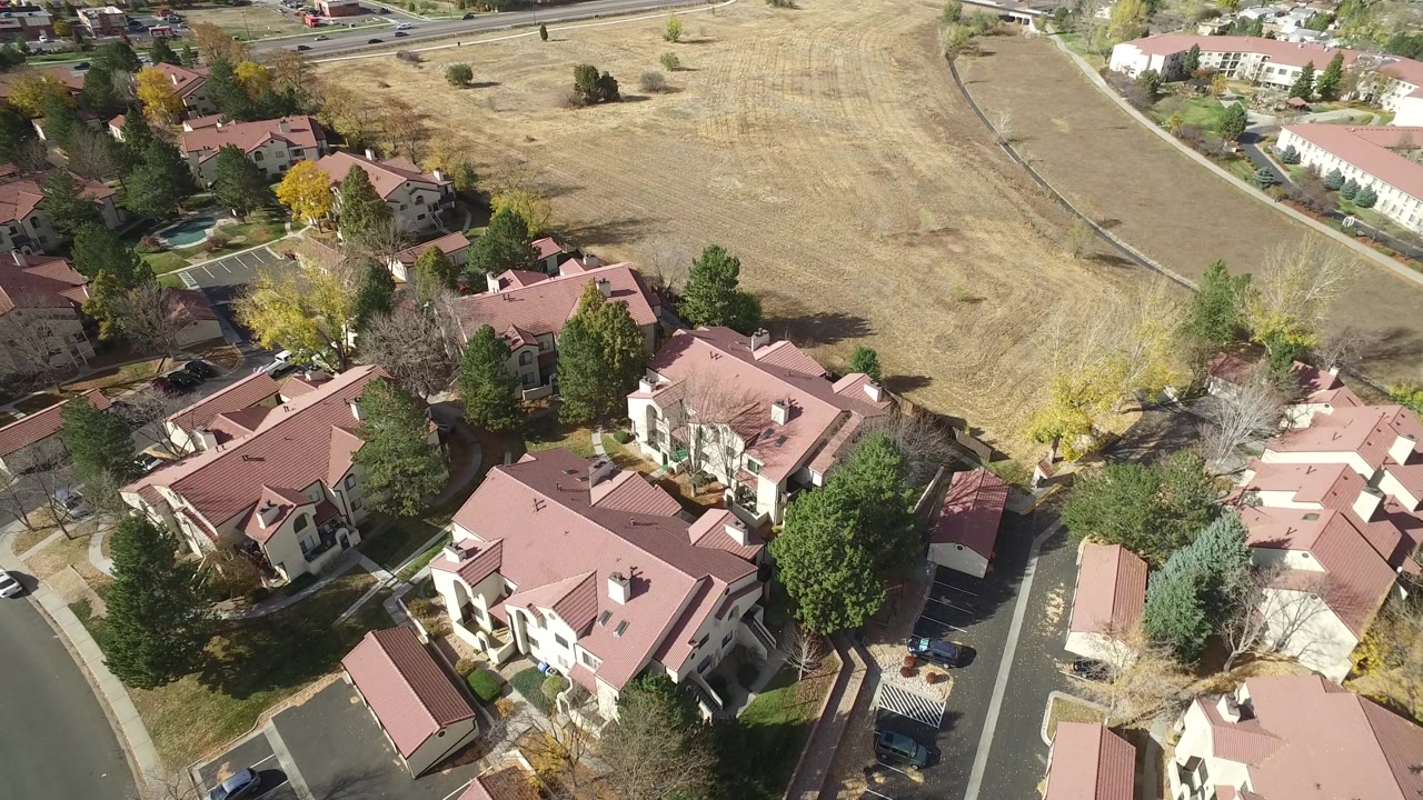 Aerial frame in Hidden Lake, Colorado with red roofs filling the lower half, trees around the residences, and a pale open field across the upper frame, with no visible people.